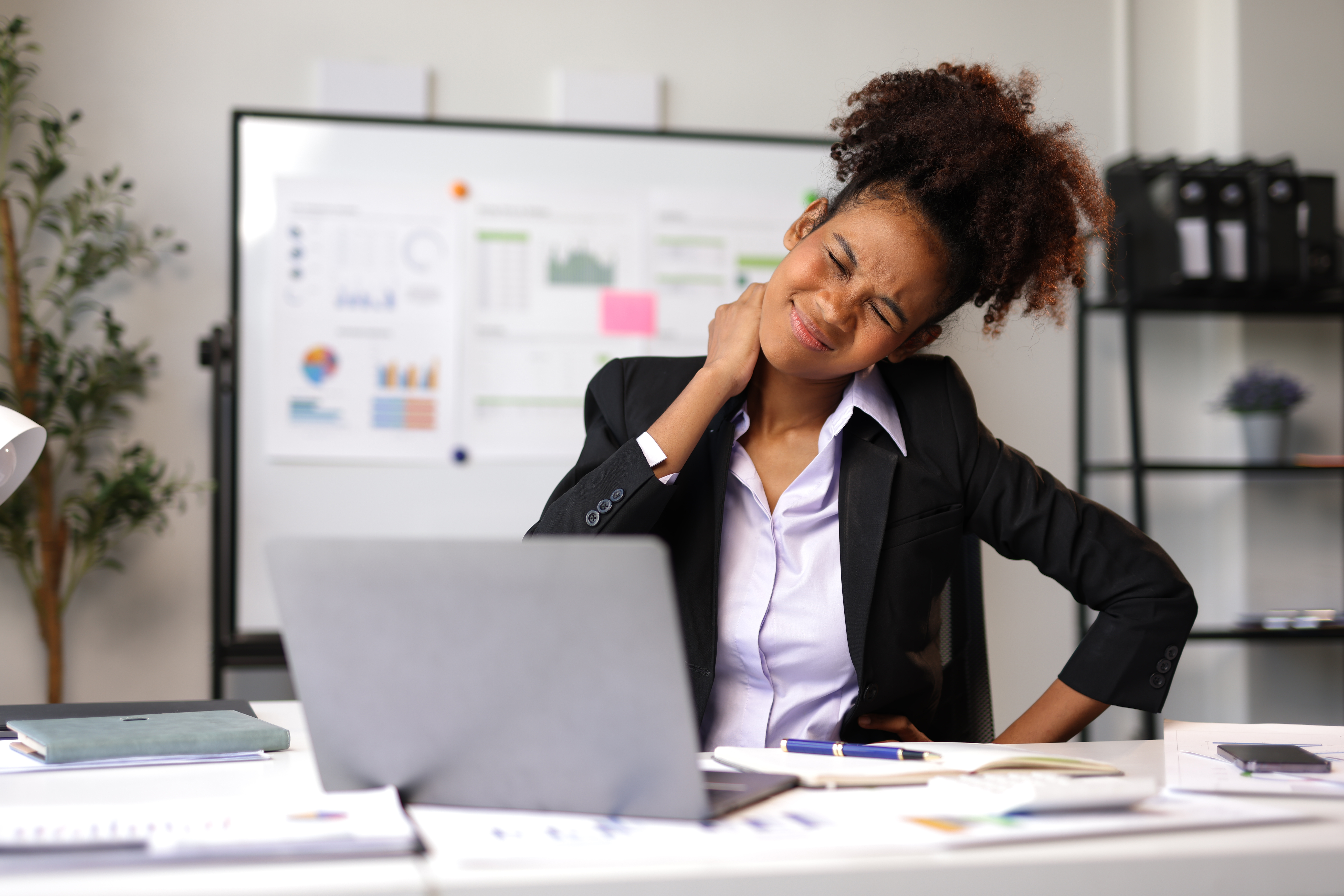 Young African American manager touching her neck and feeling strong pain while sitting at workplace with laptop, suffering from office syndrome.